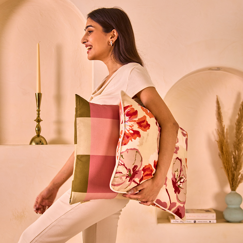 A woman carrying two cusion covers made from hemp fabric, featuring a checkered pattern and a floral print in a cozy interior.