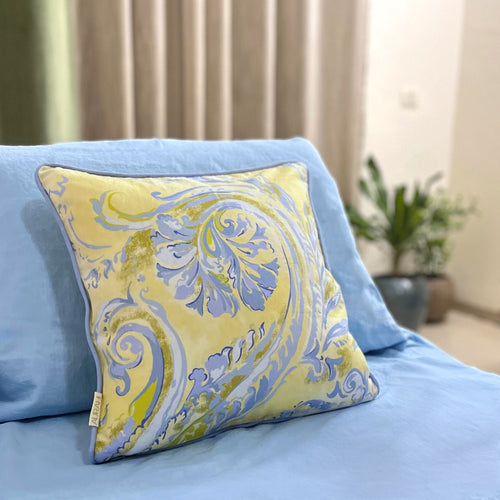 A yellow and blue floral cusion cover made from hemp fabric, displayed on a light blue bed in a softly styled room.
