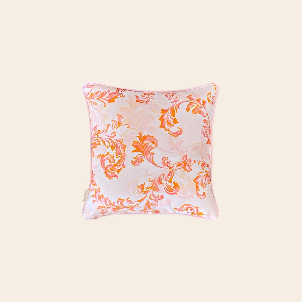A vibrant orange and pink cushion cover made from hemp fabric, featuring an intricate floral scrollwork pattern on a light base, centered against a clean off-white background.
