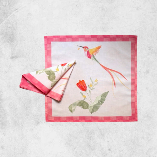 An organic Eira table napkin featuring a hand-painted hummingbird and botanical floral design with a red checkered border.