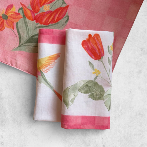 Hand-painted table napkin with a vibrant hummingbird and botanical flower motif, finished with a decorative red checkered border.